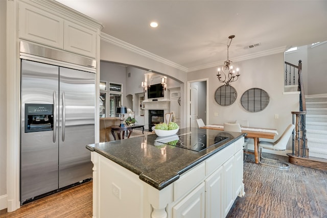 kitchen featuring light wood finished floors, black electric cooktop, stainless steel built in fridge, arched walkways, and white cabinets