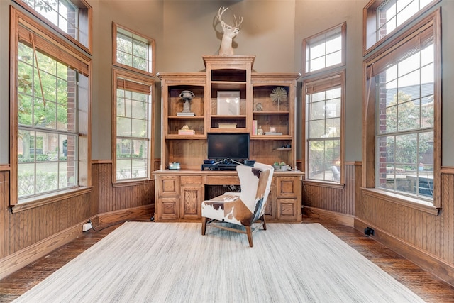 office area with a high ceiling, wainscoting, wood walls, and wood finished floors