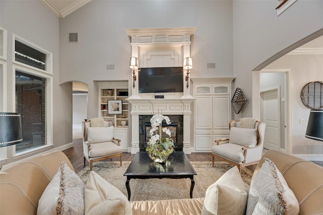 living room with visible vents, arched walkways, ornamental molding, wood finished floors, and a high ceiling