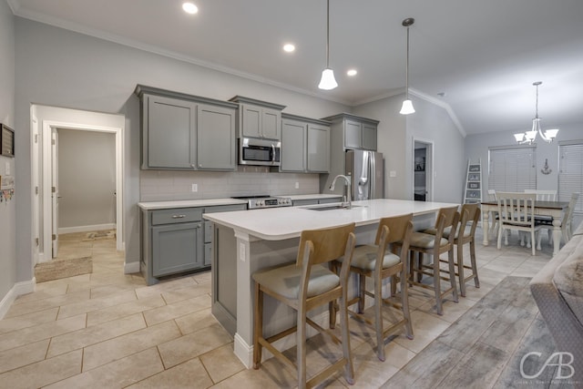 kitchen with an island with sink, stainless steel appliances, a sink, gray cabinetry, and crown molding