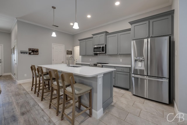 kitchen with a sink, gray cabinetry, stainless steel appliances, ornamental molding, and an island with sink