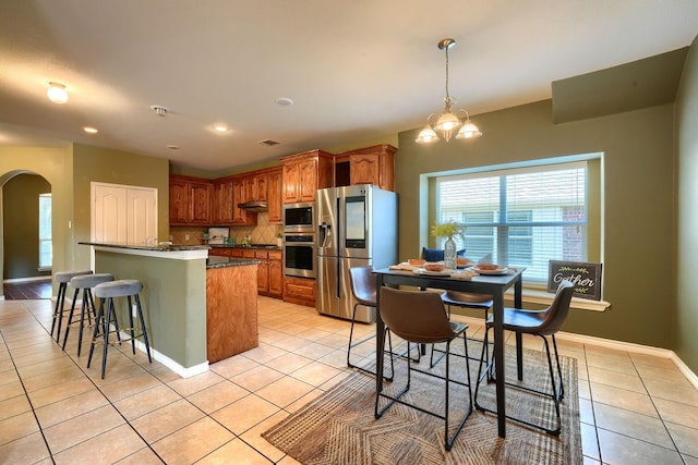 kitchen featuring light tile patterned floors, a wealth of natural light, dark countertops, arched walkways, and appliances with stainless steel finishes