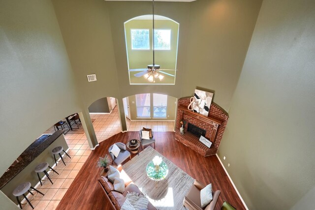 living area featuring ceiling fan, arched walkways, a fireplace, wood finished floors, and a high ceiling