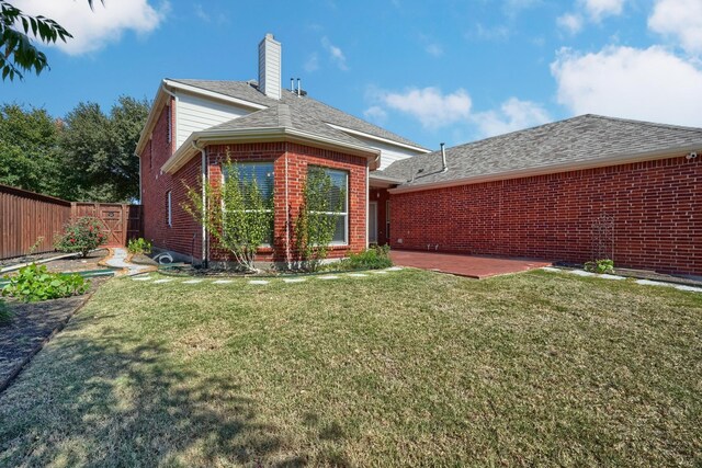 rear view of house with a chimney, brick siding, fence, a patio area, and a lawn