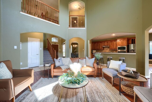 living room featuring a high ceiling, stairway, baseboards, arched walkways, and wood finished floors