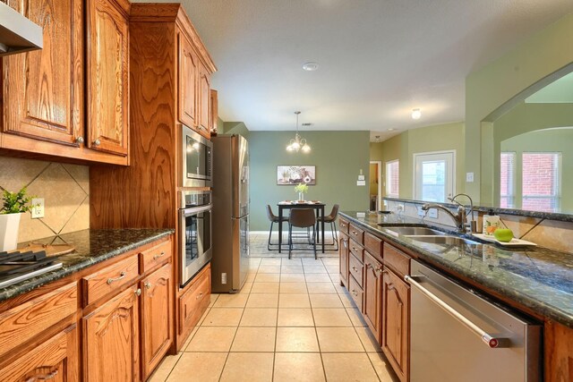 kitchen featuring dark stone countertops, brown cabinets, a sink, appliances with stainless steel finishes, and backsplash