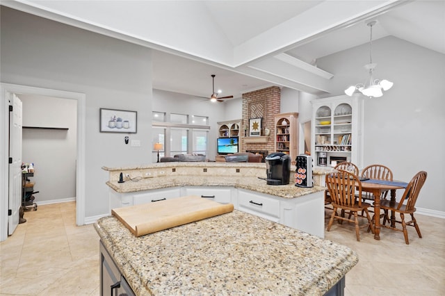 kitchen with lofted ceiling, white cabinetry, open floor plan, a brick fireplace, and ceiling fan with notable chandelier