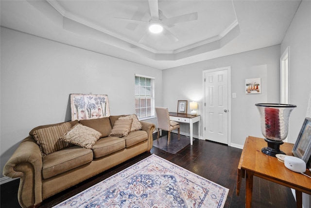 living room featuring crown molding, a tray ceiling, baseboards, dark wood finished floors, and a ceiling fan
