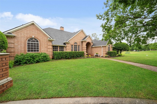 ranch-style house with a front yard, a chimney, a shingled roof, and brick siding
