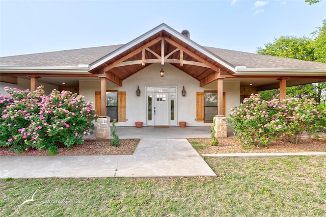 view of front facade with stucco siding, covered porch, and a shingled roof