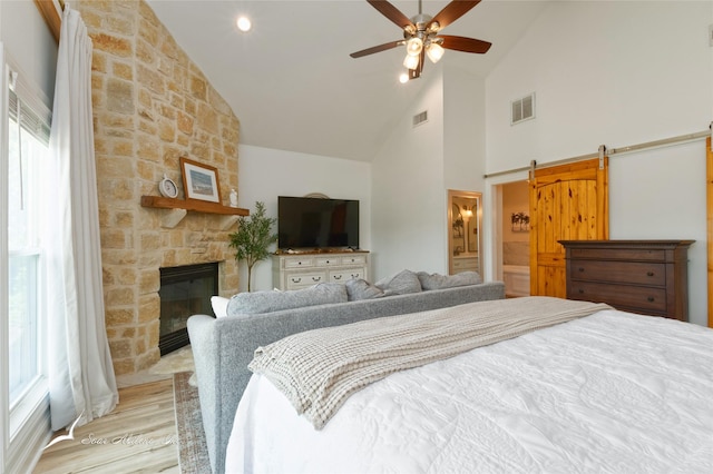 bedroom featuring visible vents, a fireplace, light wood finished floors, and high vaulted ceiling