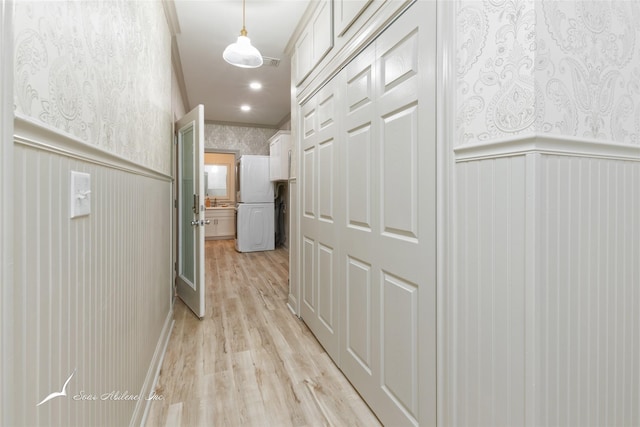 hallway with wallpapered walls, wainscoting, a decorative wall, and light wood-style floors