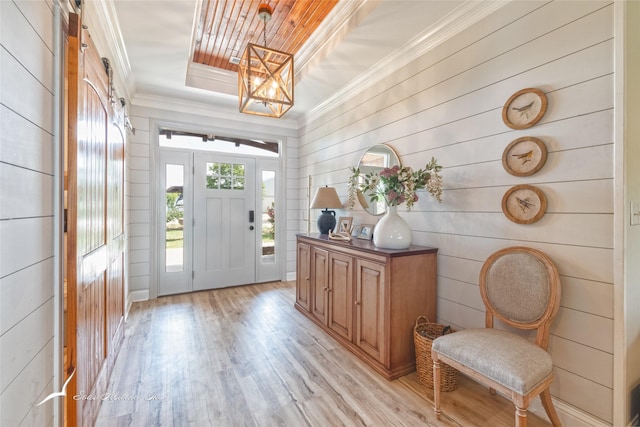 foyer entrance featuring wood walls, a raised ceiling, ornamental molding, and light wood-style flooring