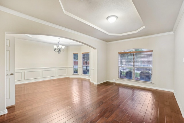 empty room featuring a chandelier, a raised ceiling, arched walkways, and dark wood-type flooring