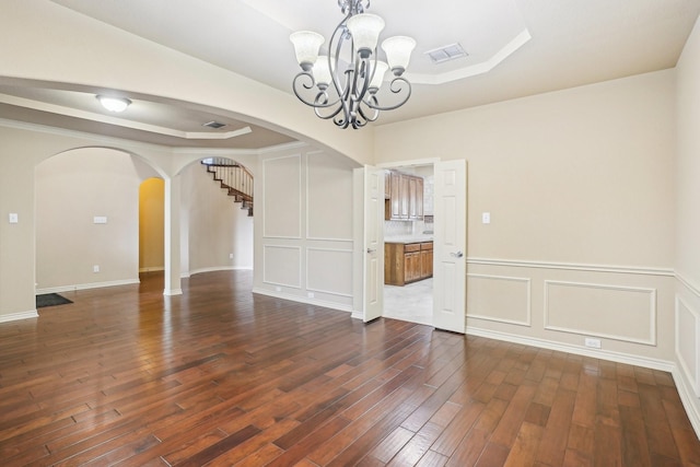 unfurnished dining area featuring arched walkways, dark wood-style floors, visible vents, a raised ceiling, and a notable chandelier