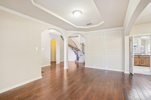 unfurnished living room with stairway, a raised ceiling, visible vents, arched walkways, and dark wood finished floors