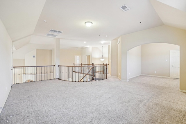unfurnished room featuring light colored carpet, visible vents, lofted ceiling, and arched walkways