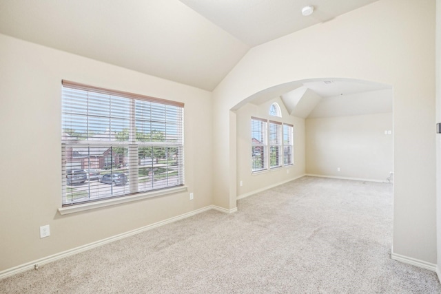 carpeted spare room with baseboards, arched walkways, and vaulted ceiling