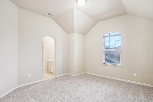 empty room featuring arched walkways, light colored carpet, vaulted ceiling, baseboards, and visible vents