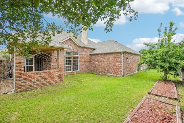 rear view of house with brick siding, a chimney, a lawn, roof with shingles, and fence