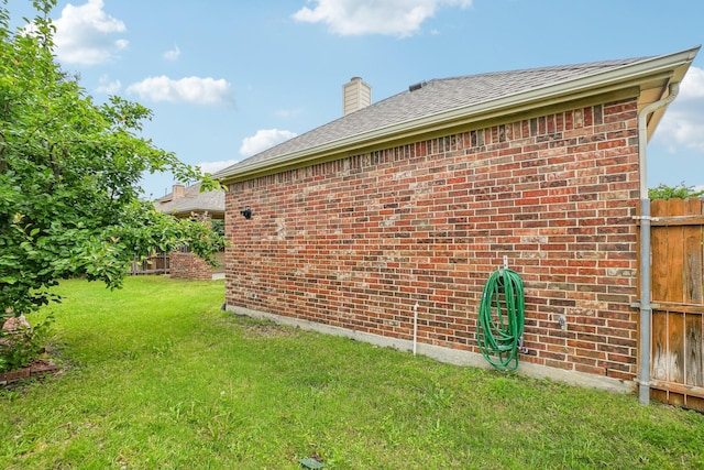 view of home's exterior featuring fence, a chimney, a yard, and brick siding
