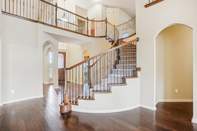 stairs featuring hardwood / wood-style floors, baseboards, arched walkways, and a high ceiling
