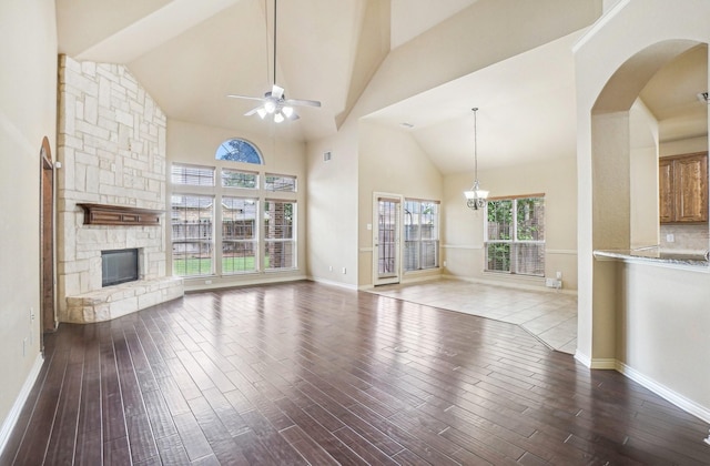 unfurnished living room with wood finished floors, high vaulted ceiling, a stone fireplace, and ceiling fan with notable chandelier