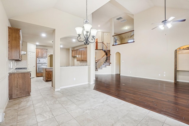 unfurnished dining area with stairway, arched walkways, light wood finished floors, high vaulted ceiling, and ceiling fan with notable chandelier