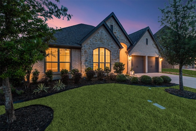 french country inspired facade featuring a front yard, driveway, stone siding, and an attached garage