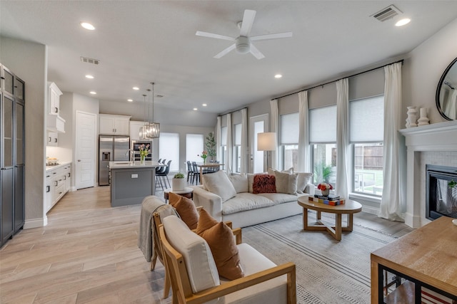 living room with visible vents, light wood-type flooring, a tile fireplace, and ceiling fan