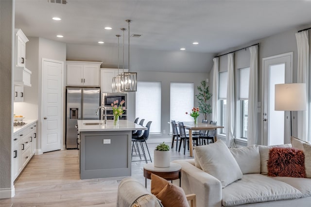 kitchen with a kitchen island with sink, stainless steel appliances, light wood-style floors, light countertops, and white cabinets