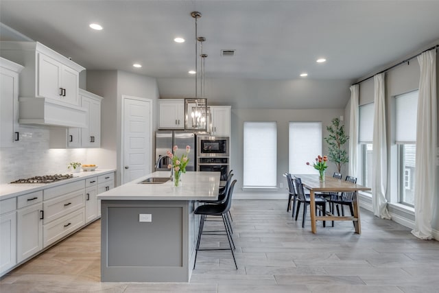 kitchen with decorative backsplash, a sink, appliances with stainless steel finishes, visible vents, and a center island with sink