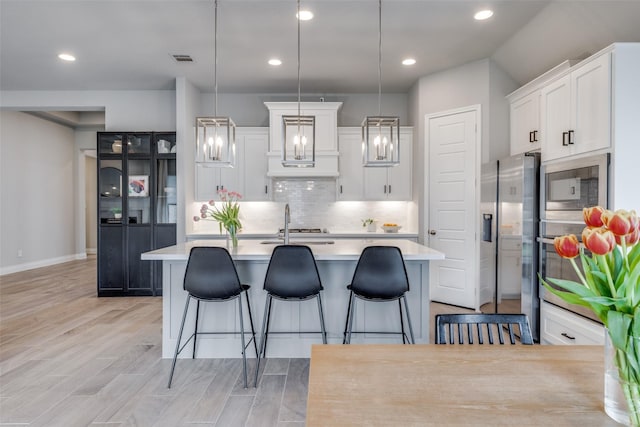 kitchen featuring stainless steel appliances, a kitchen breakfast bar, backsplash, light countertops, and white cabinets