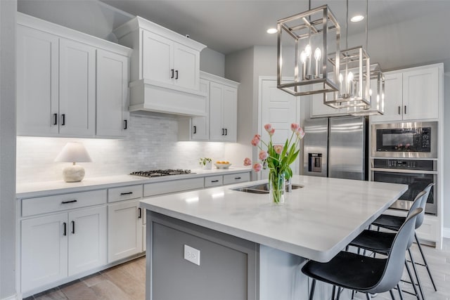 kitchen with white cabinets, appliances with stainless steel finishes, an island with sink, and light countertops
