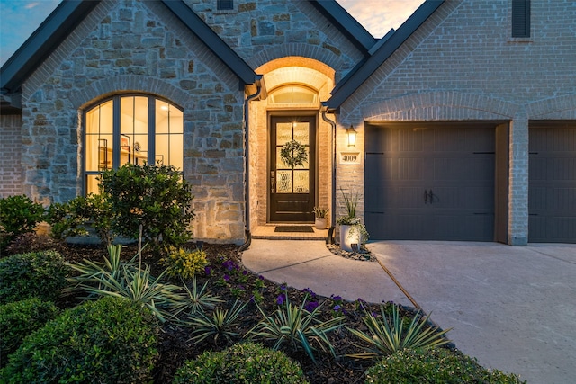entrance to property with driveway, an attached garage, and stone siding