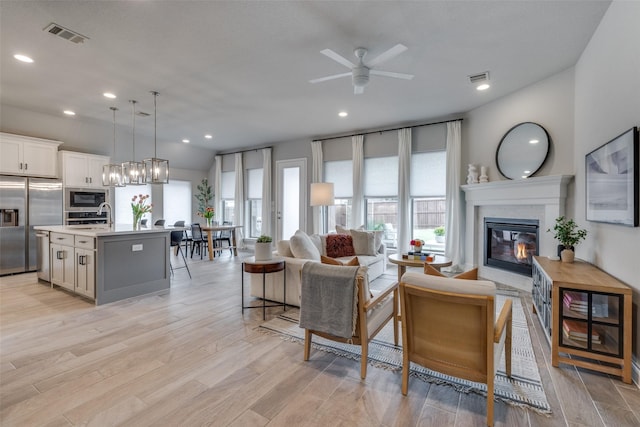 living room with a glass covered fireplace, a ceiling fan, visible vents, and plenty of natural light
