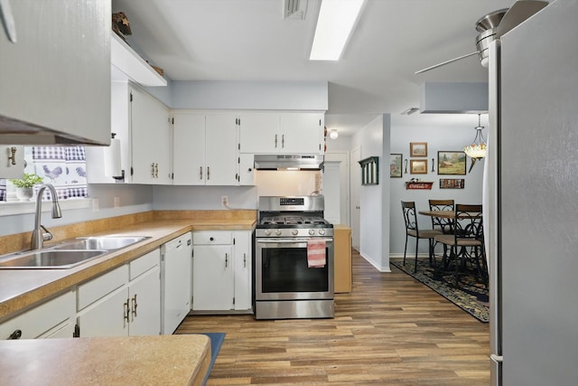 kitchen featuring wood finished floors, appliances with stainless steel finishes, white cabinets, a sink, and ventilation hood