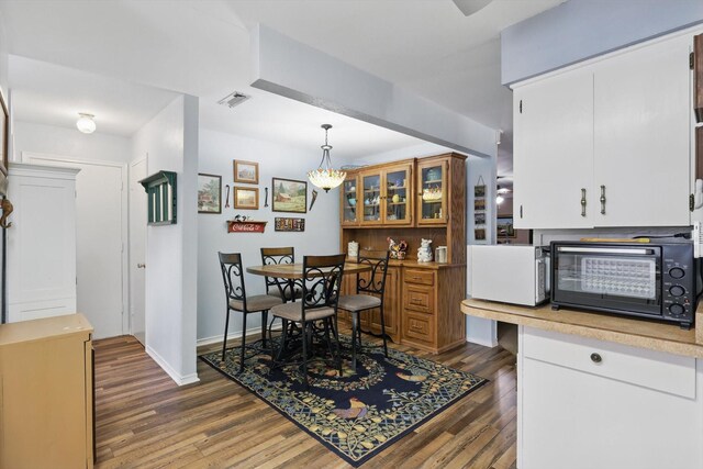 dining area with dark wood-style floors, a toaster, visible vents, and baseboards