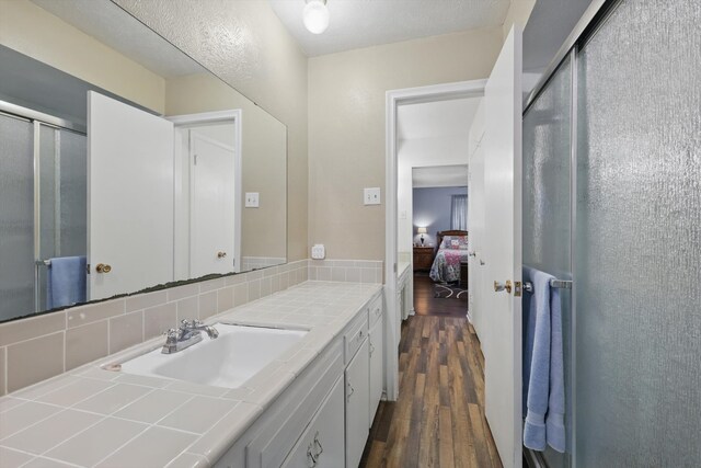 ensuite bathroom featuring tasteful backsplash, a stall shower, wood finished floors, vanity, and ensuite bath