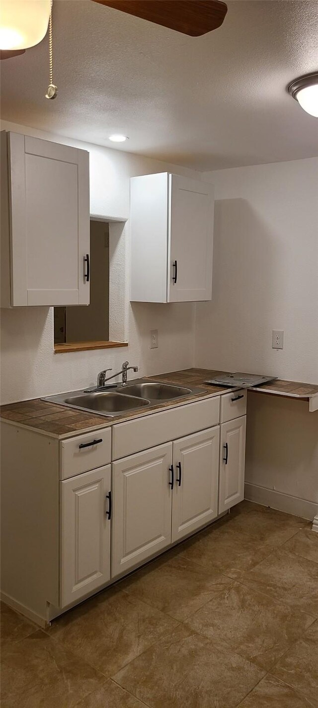 kitchen featuring a textured ceiling, white cabinets, and a sink