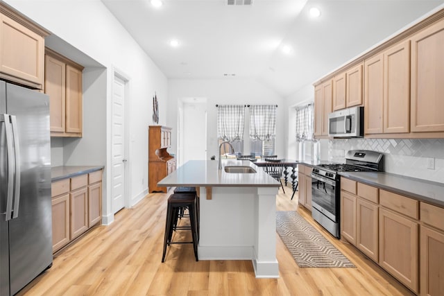 kitchen with tasteful backsplash, a sink, appliances with stainless steel finishes, light brown cabinets, and vaulted ceiling