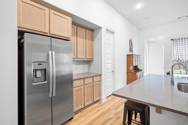kitchen with a sink, light brown cabinets, visible vents, stainless steel refrigerator with ice dispenser, and light wood-style flooring