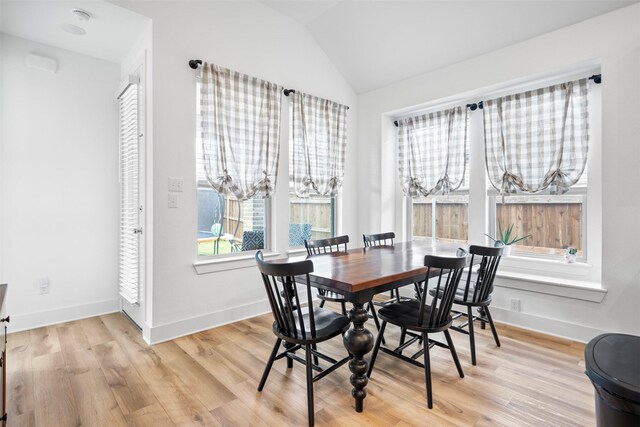 dining room with light wood finished floors, lofted ceiling, and baseboards