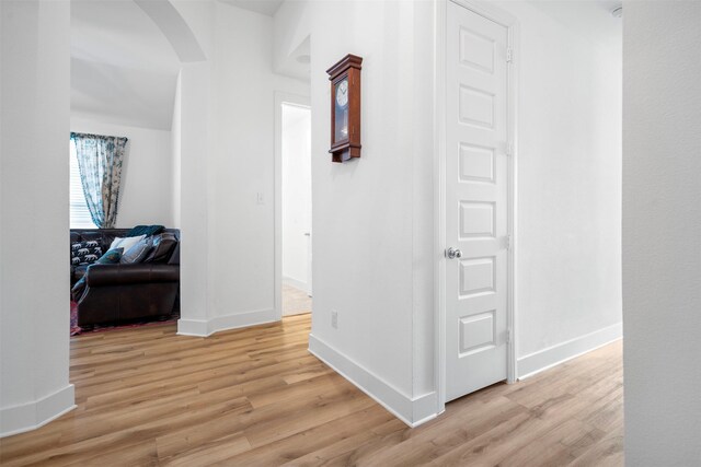 hallway featuring light wood-type flooring, baseboards, and arched walkways