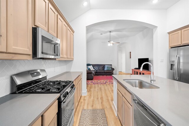 kitchen featuring arched walkways, light brown cabinets, appliances with stainless steel finishes, a sink, and light wood-type flooring