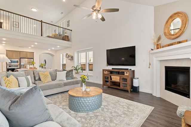 living room featuring arched walkways, ceiling fan, a fireplace, high vaulted ceiling, and dark wood-type flooring
