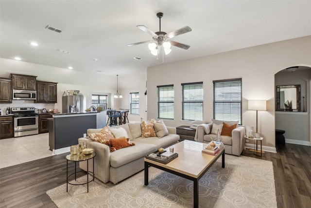 living area featuring arched walkways, a ceiling fan, visible vents, and light wood-type flooring