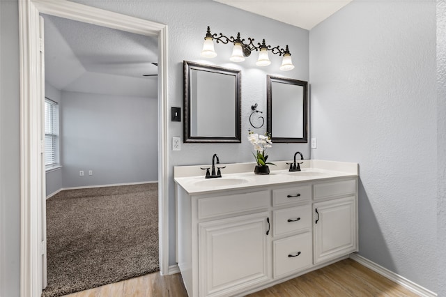 full bath with double vanity, wood finished floors, baseboards, and a sink
