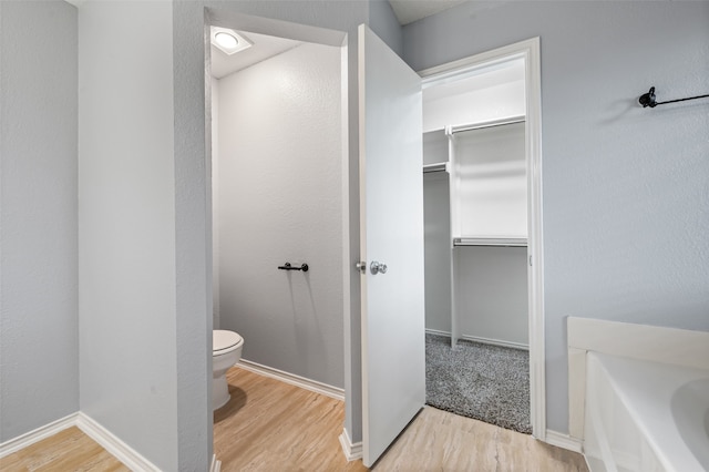 bathroom featuring a spacious closet, wood finished floors, toilet, and a bath