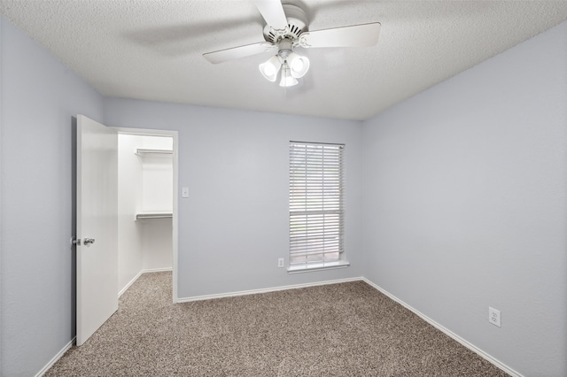 unfurnished bedroom with a textured ceiling, a closet, baseboards, carpet floors, and a walk in closet